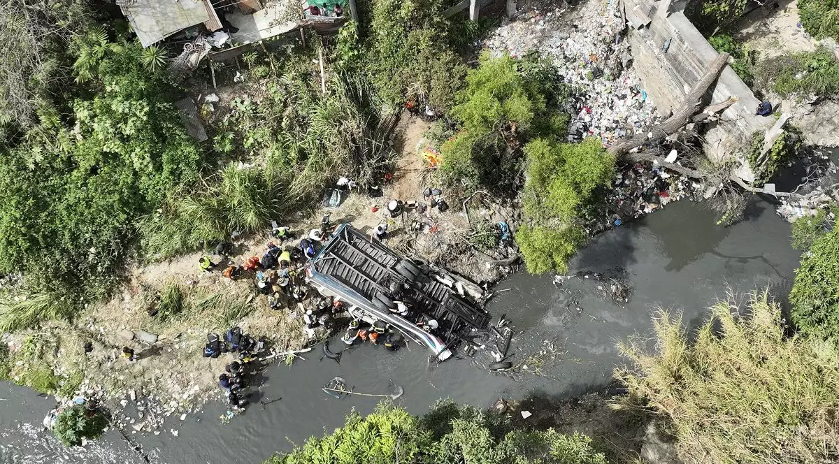 Un autobuz răsturnat se vede în albia unui râu, înconjurat de oameni