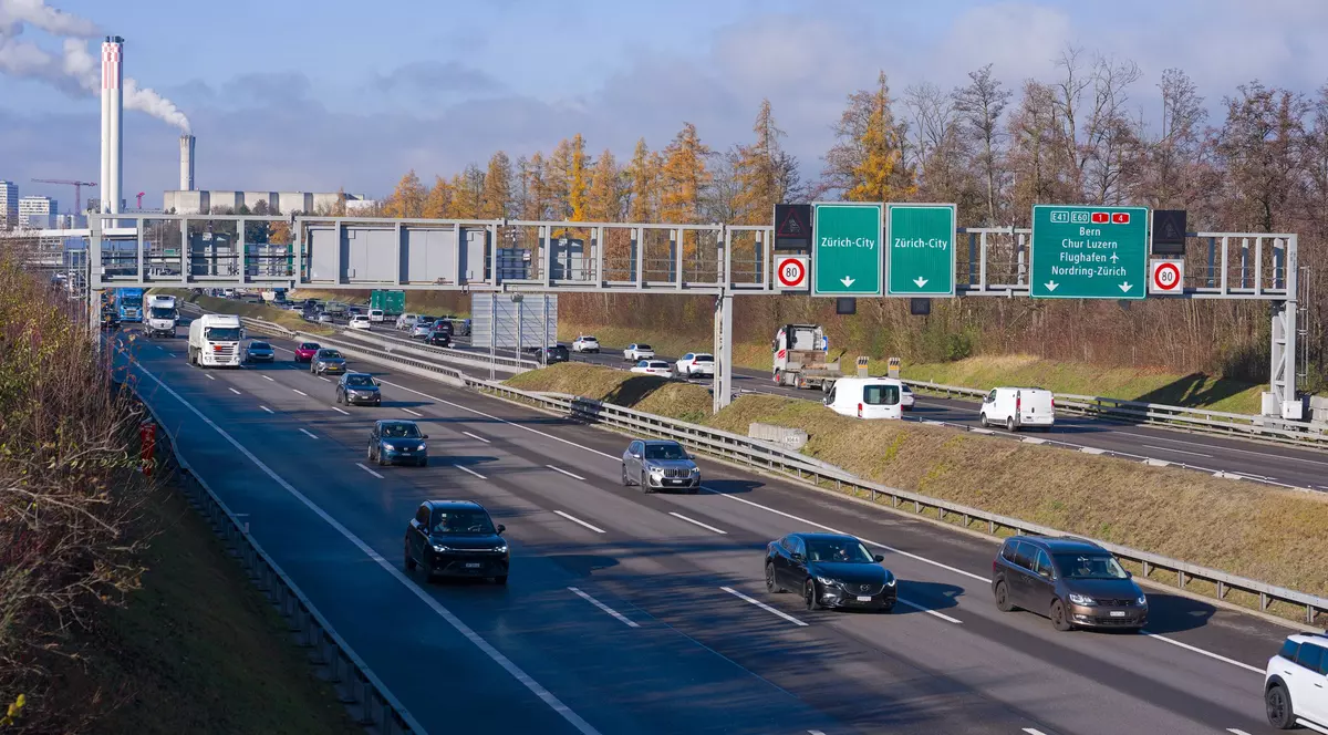 autostradă din Elveția, în apropierea orașului Zurich pe care circula mai multe masini si camioane. in dreapta se observa indicatoare rutiere care indica directia pentru orasul zurich