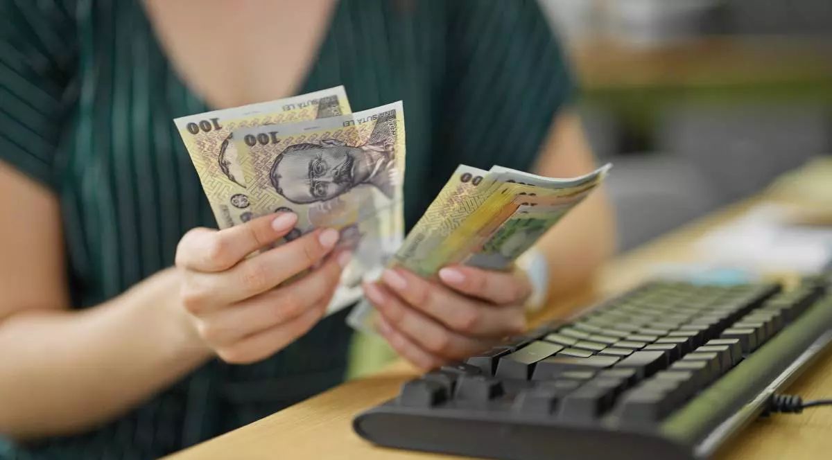 femeie care numara mai multe bancnote romanesti in fata ei are o tastatura de calculator