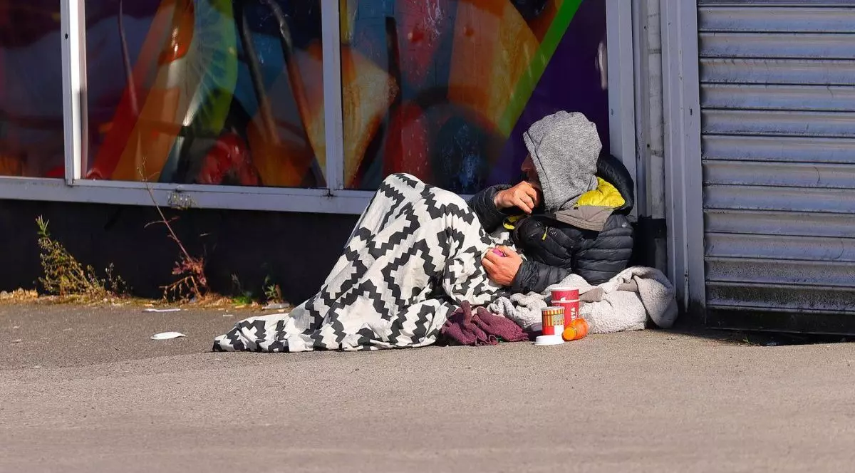 Cerșetor din Anglia, întrins pe stradă. Se apără de frig cu o pătură și are o sticlă cu alcool cu el