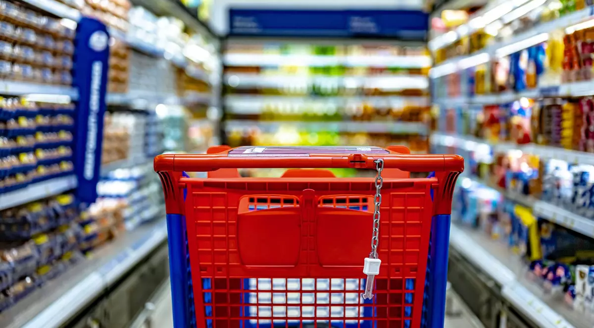 Un coș de cumpărături roșu se vede pe culoarul unui supermarket