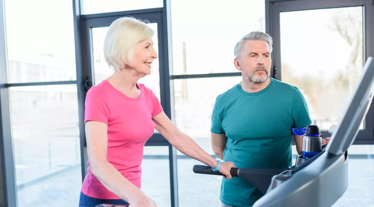 O femeie care merge pe banda, în stânga, îmbrăcată într-un tricou roz, un bărbat care o priveste, îmbrăcat în tricou verde, in dreapta