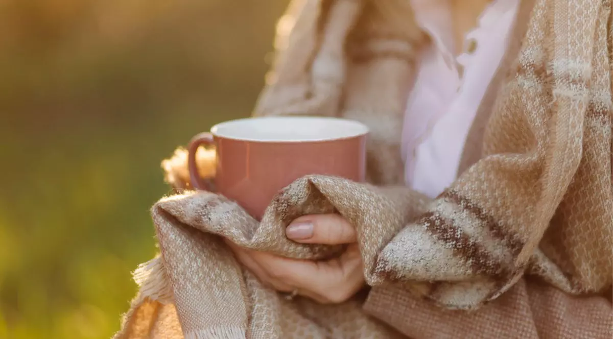 femeie în pătură cu model cu dungi care ține în mână o cană de ceai roz