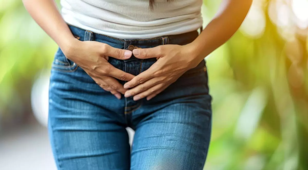 Imagine creativă cu o femeie care suferă de balonare, îmbrăcată în blugi de culoare albastră și o bluză de culoare albă, pe fundal verde