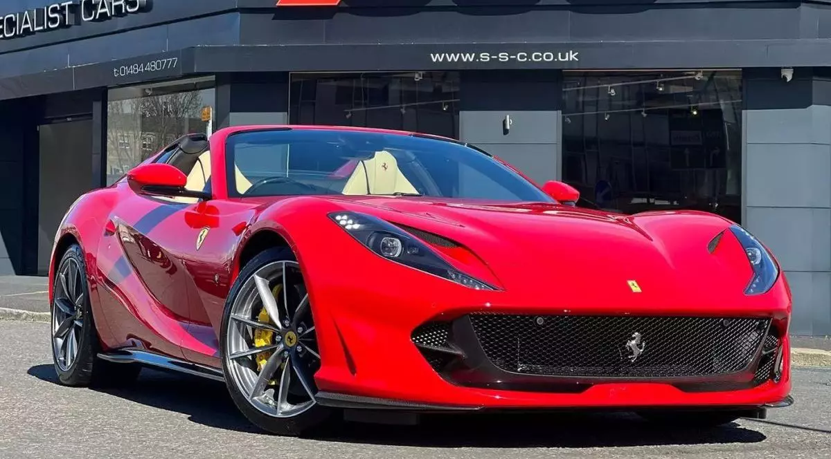 O mașină roșie Ferrari 812 GTS Spider F1 de lux stă parcată pe o stradă, în fața unui magazin