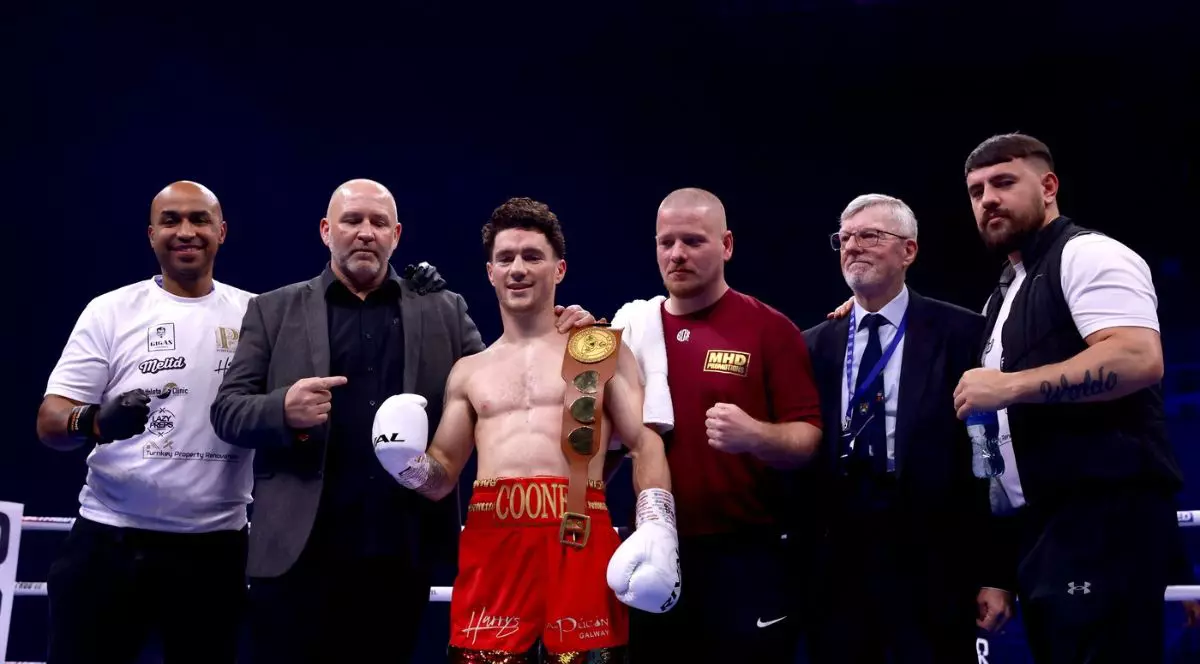 Fotografie de arhivă datată 251123 a boxerului irlandez John Cooney (centru), îmbrăcat într-o pereche de pantaloni scurți roșii cu o banderola pe care este scris numele său, alături de staff și antrenori