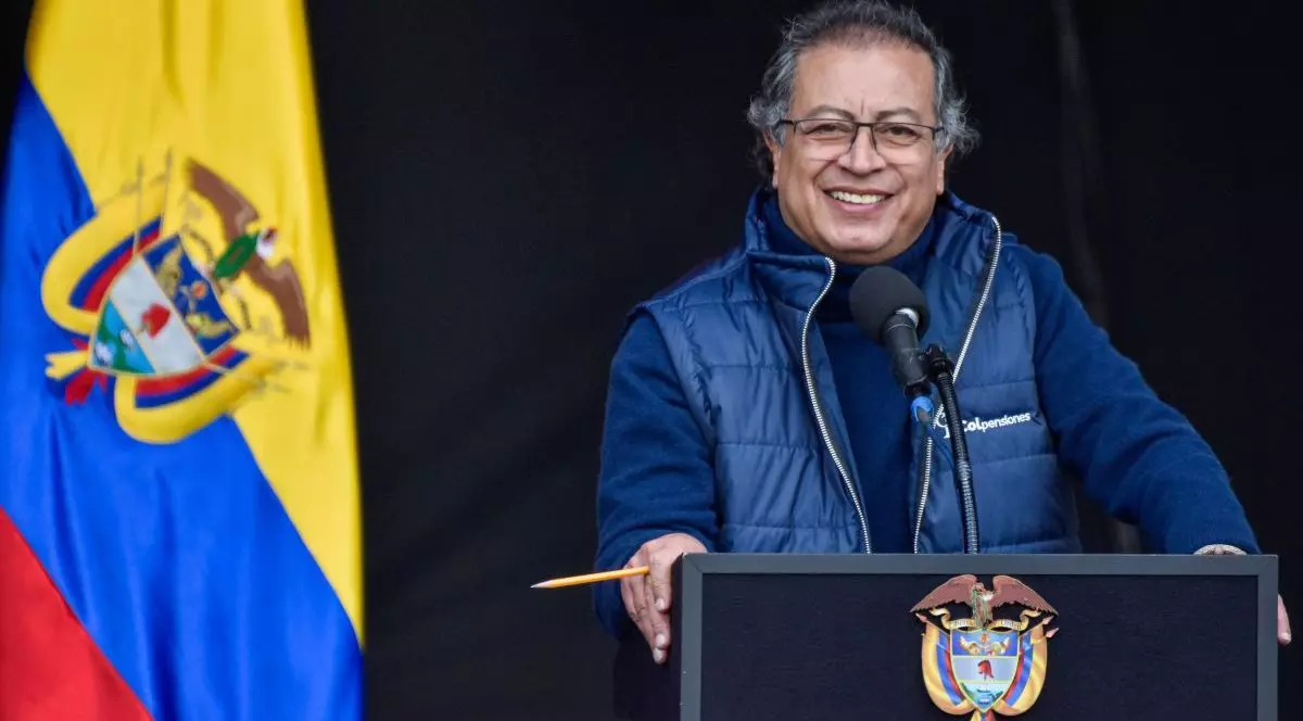 Președintele Columbiei, Gustavo Petro, îmbrăcat cu o vestă bleumarin și un hanorac pe dedesubt, vorbește zâmbind de la tribună. În stânga imaginii este drapelul țării, iar în spatele lui este un fond negru