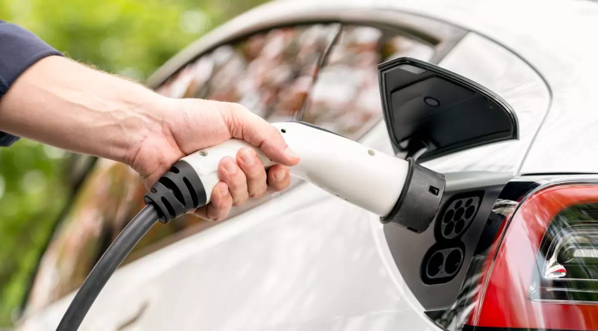 persoana care tine in mana incarcator auto langa o masina alba electrica