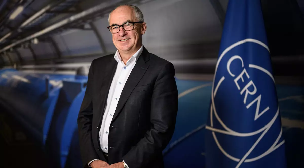 Mark Thomson, viitorul director general CERN stă lângă un steag albastru cu logo-ul organizației.