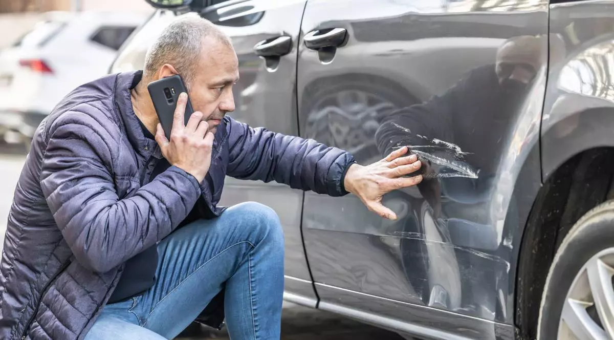un barbat care sta langa masina lovita in parcare vorbind la telefon