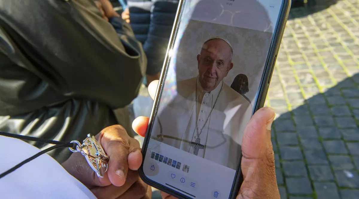 Persoană necunoscută ține în mână un telefon mobil cu o fotografie a Papei Francisc în Piața Sfântul Petru din Vatican