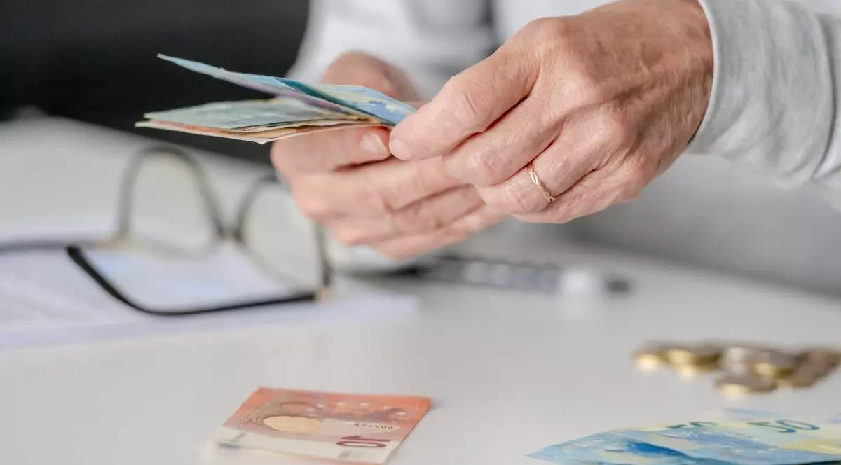 mainile unui batran care numara cateva bancnote in euro