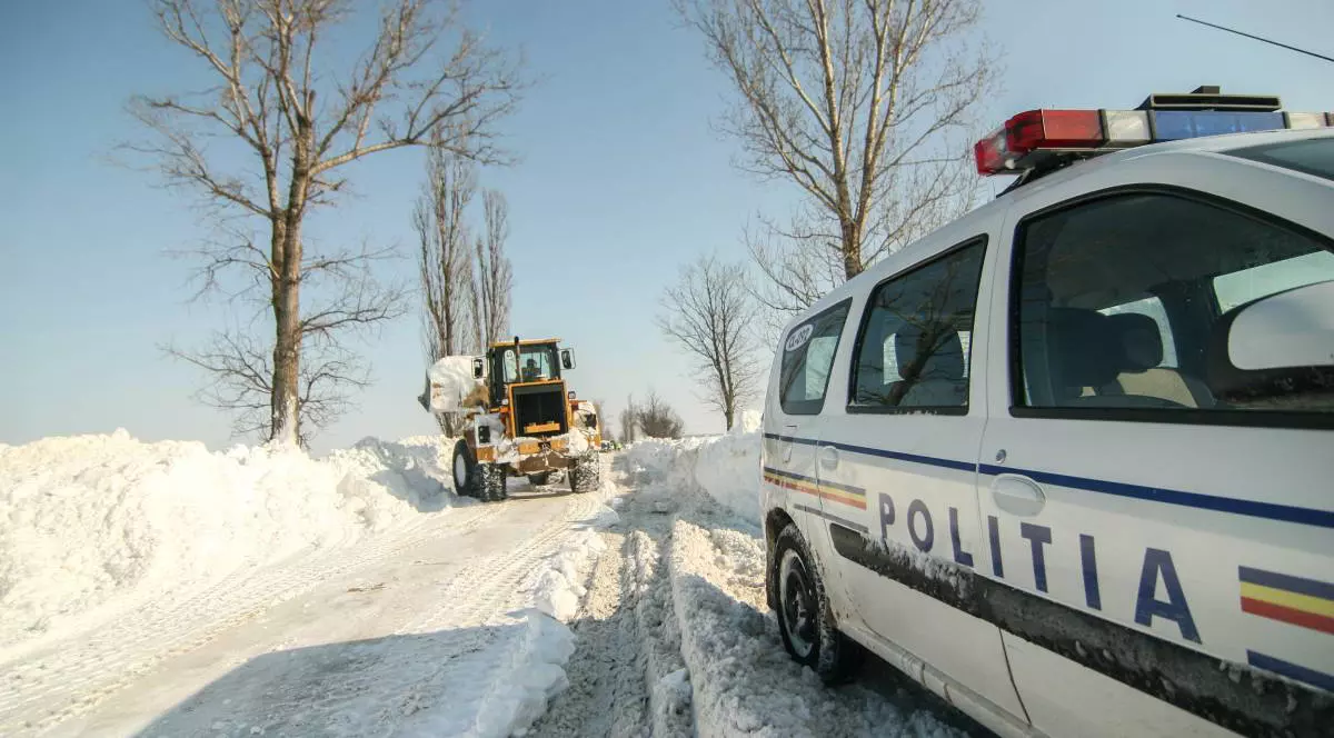 masina politiei romane pe un drum inzapezit, in spate se observa un utilaj de deszapezire