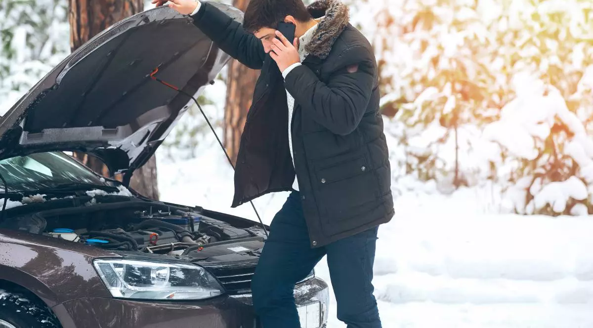 barbat care sta langa masina cu capota deschisa vorbind la telefon, se observa ca este intr-o zona in care a nins foarte mult