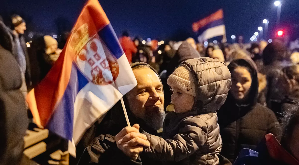 Un părinte își poartă în brațe copilul și flutură împreună un steag al Serbiei, la protestul anticorupție din Belgrad