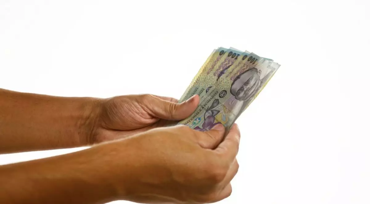 Mâinile unui bărbat care țin mai multe bancnote românești de 100 de lei, pe un fundal alb