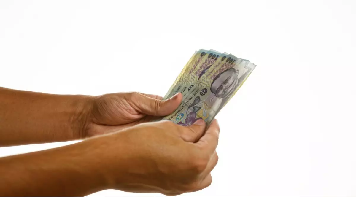 Mâinile unui bărbat care țin mai multe bancnote românești de 100 de lei, pe un fundal alb