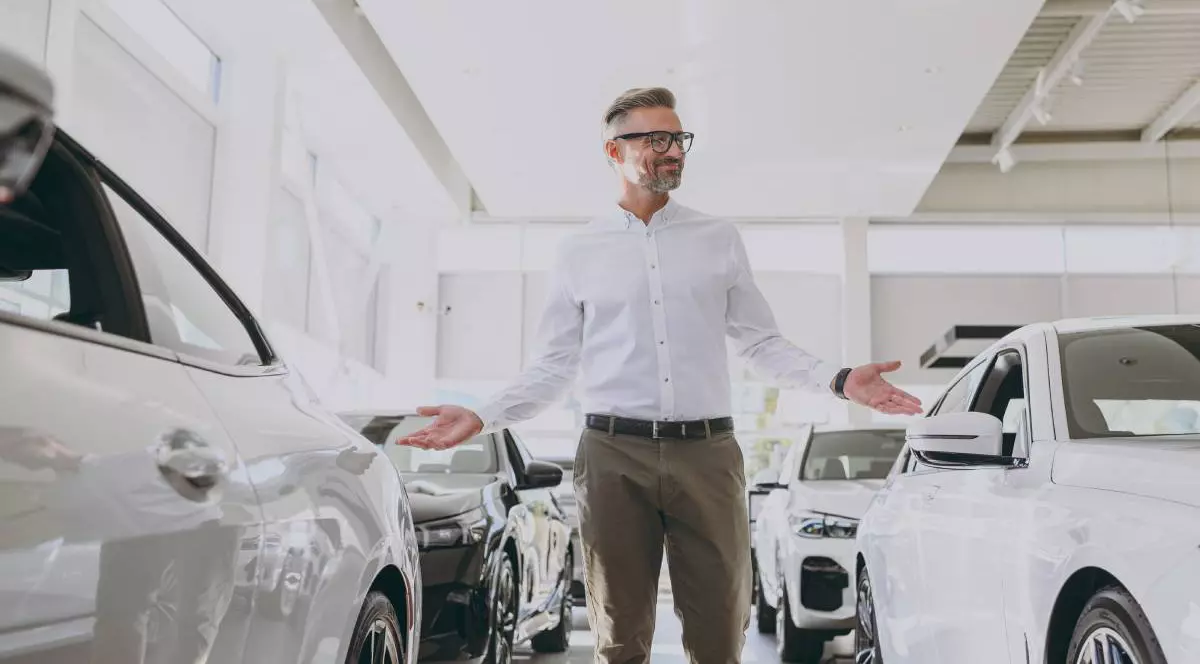 barbat imbracat cu o camasa alba aflat printre mai multe masini intr-un showroom auto