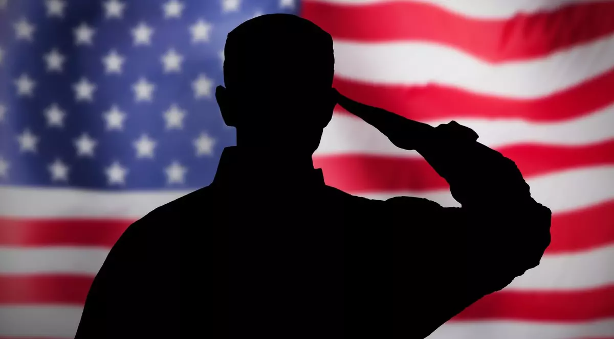 Poză cu un soldat care salută, iar pe fundal este steagul SUA