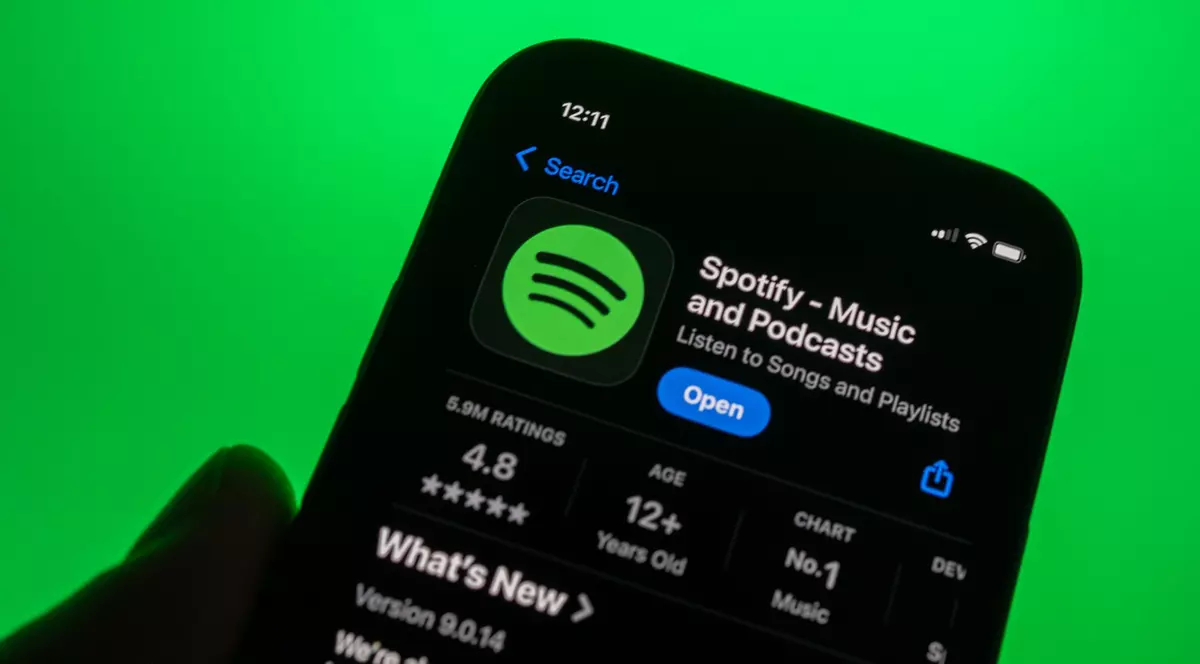 Pagina aplicației SPotify din AppStore, deschisă pe ecranul unui iPhone ținut în mână în fața unui fundal verde.
