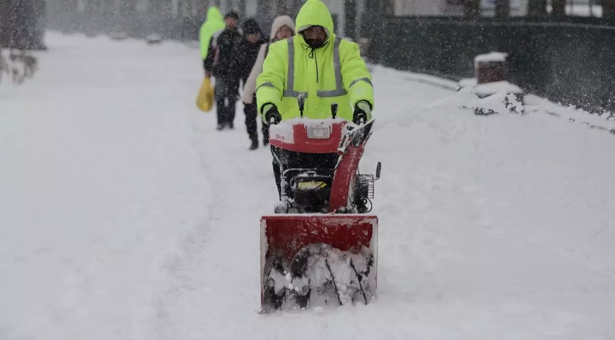 Un lucrător de la deszăpezire, cu o haină verde deschis, înlătură stratul de zăpadă de pe stradă, iar în spatele lui merg alte persoane. Foto: Libertatea/Vlad Chirea