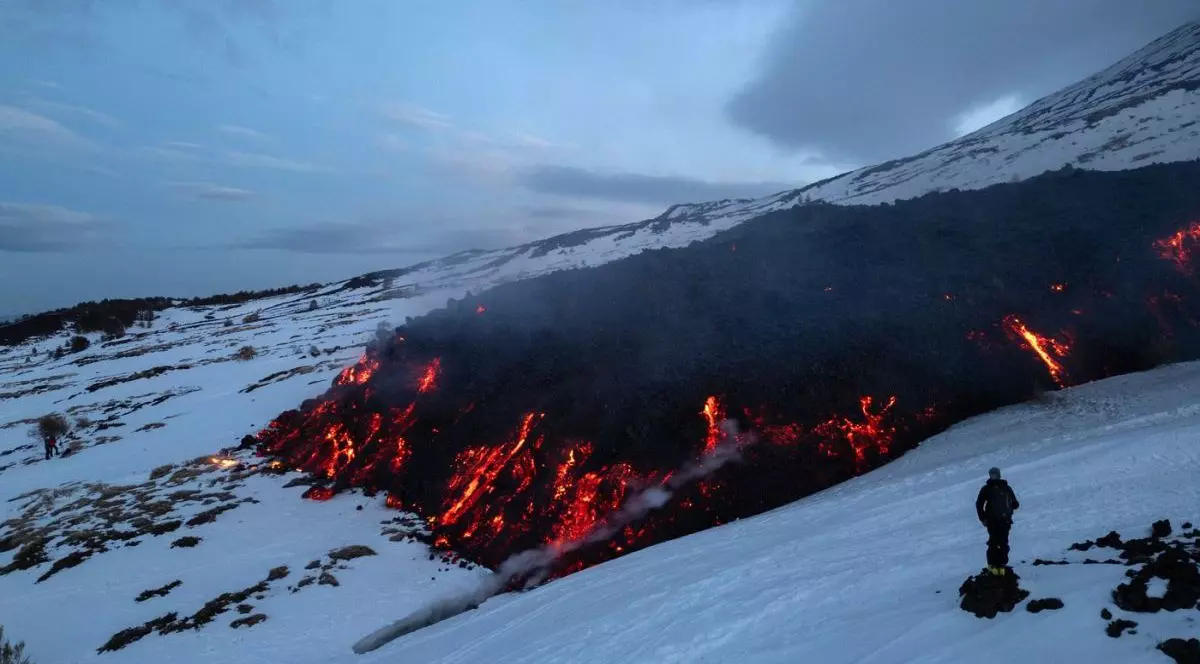 Un turist se uită la lava care curge de pe Muntele Etna în timpul unei erupții a vulcanului pe 14 februarie 2025