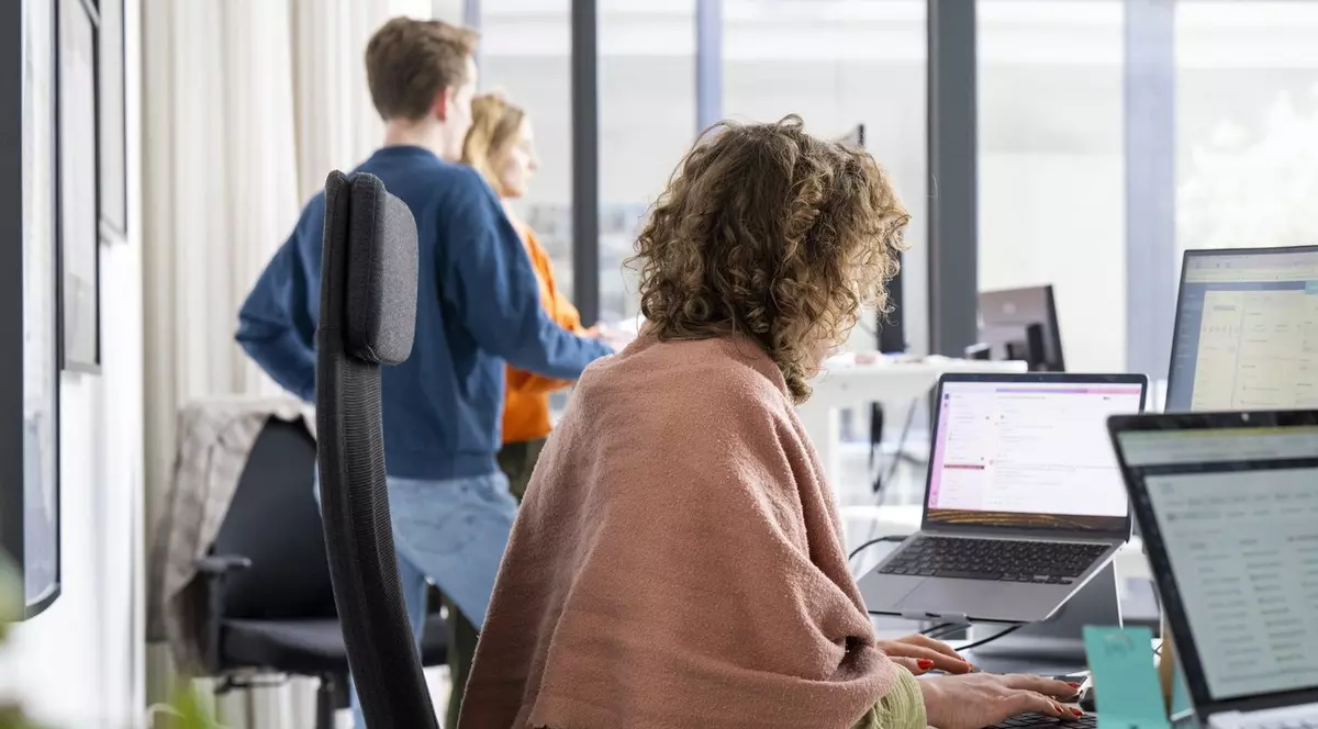 Trei lucrători de birou sunt concentrați pe ecranul computerului în timp ce lucrează într-un birou modern cu lumină naturală.