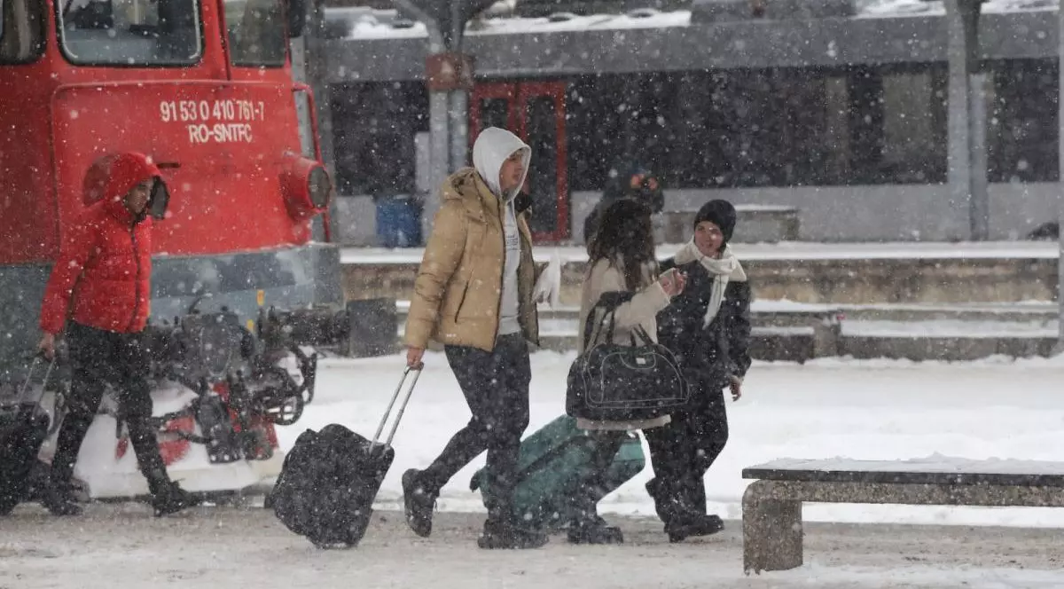 Mai mulți oameni cară bagaje în Gara de Nord din București și se vede locomotiva roșie a unui tren, într-o zi în care ninge și pe jos este zăpadă