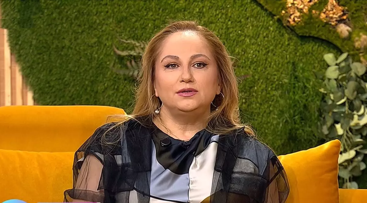 Astrologul Cristina Demetrescu stă pe o canapea portocalie, în studioul unei emisiuni, având în spate un fundal verde