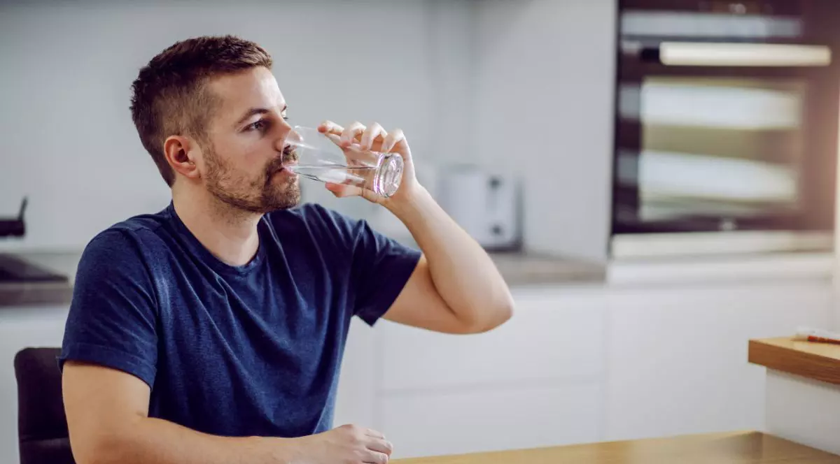 bărbat care bea un pahar cu apă în stim ce stă la masă