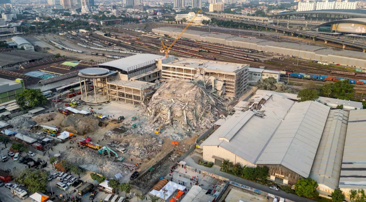 Imaginea arată o clădire prăbușită din Bangkok. În fundal, există linii de cale ferată, clădiri înalte, mașini și oameni