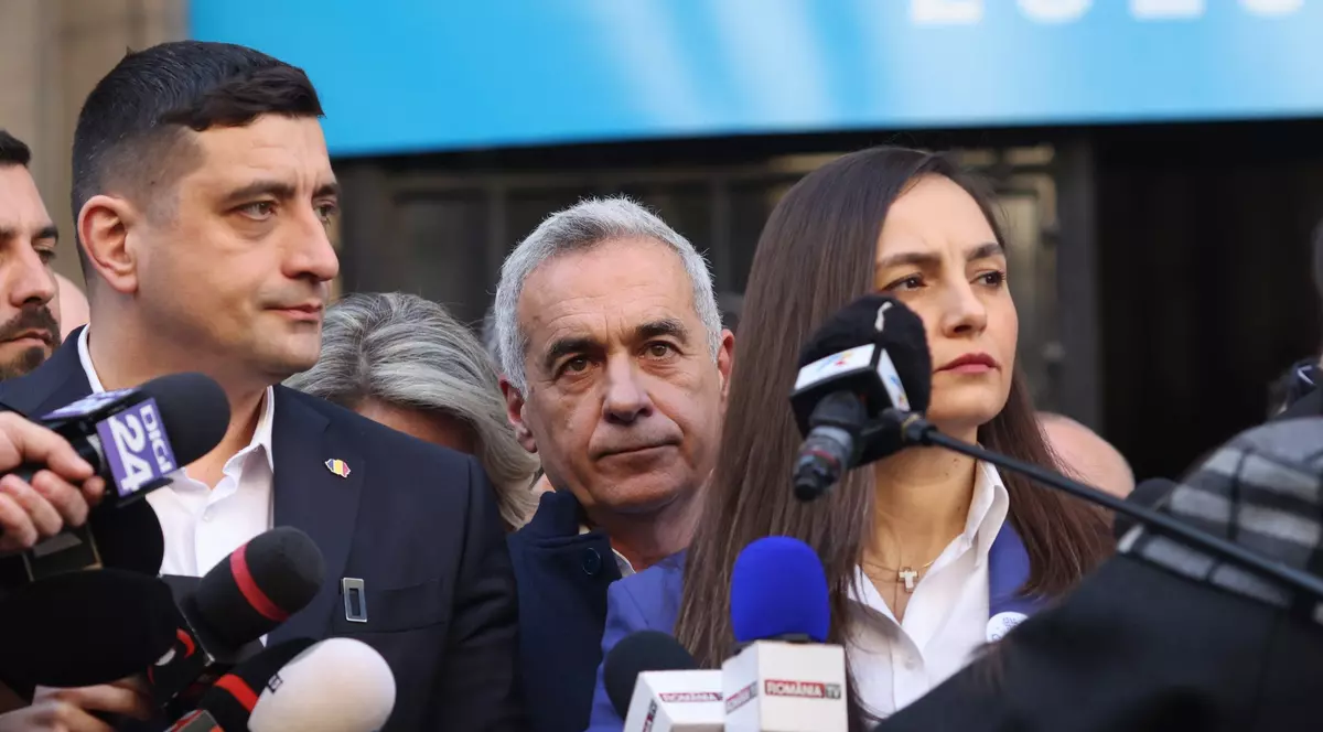 Doi bărbați și o femeie stau în fața mai multor microfoane