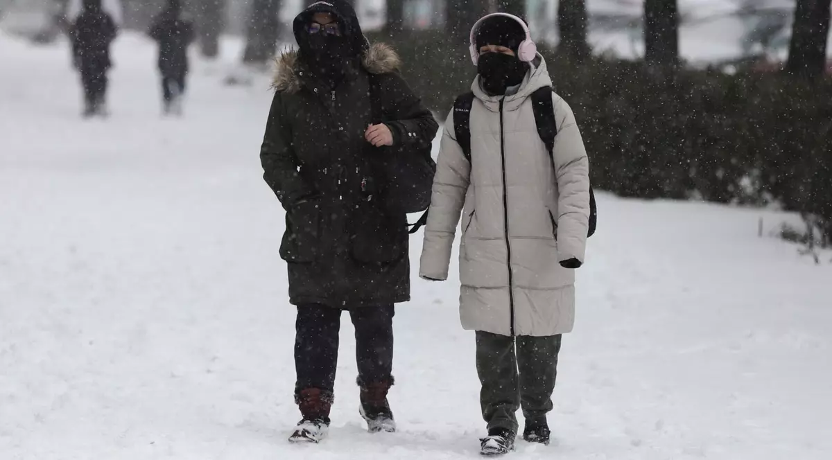 Două femei îmbrăcate cu geci groase de iarnă, cu fulare și căciuli, merg prin zăpadă, în București
