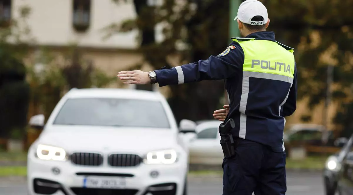 politist rutier imbracat in uniforma cu sapca alba pe cap aflat in trafic, in timp ce opreste o masina alba pe dreapta posibil pentru un control de rutina