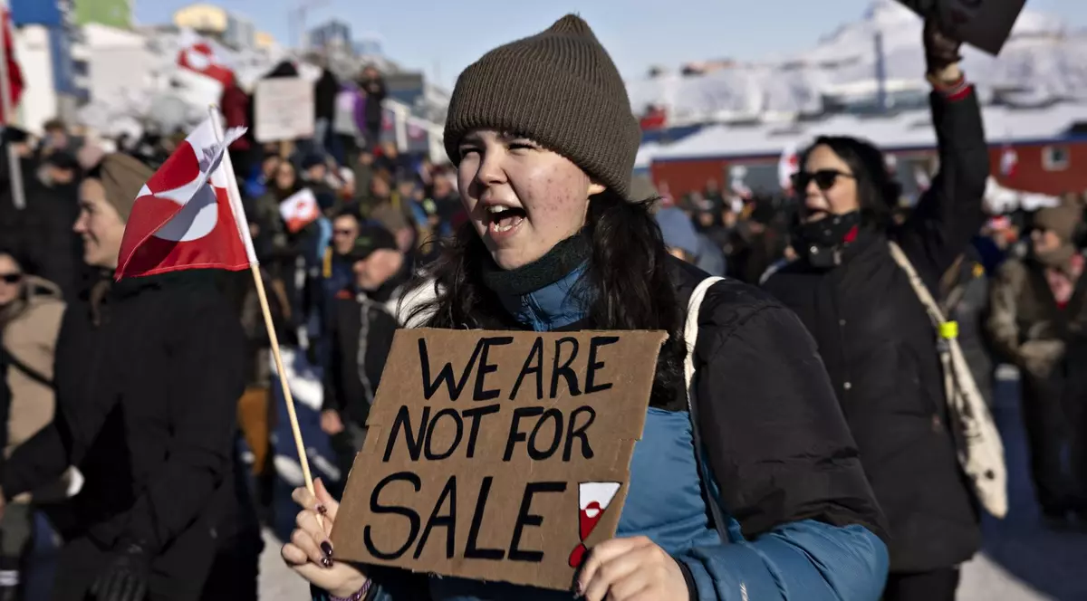 Tânără din Groenlanda care participă la un protest și care ține în mâini un panou din carton pe care scrie „Nu suntem de vânzare”