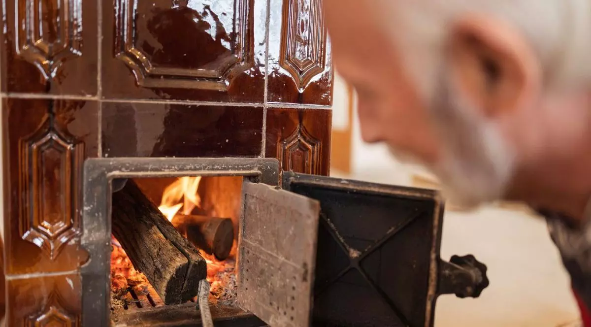 Bărbat în vârstă baga lemne într-o sobă unde ard deja alte lemne