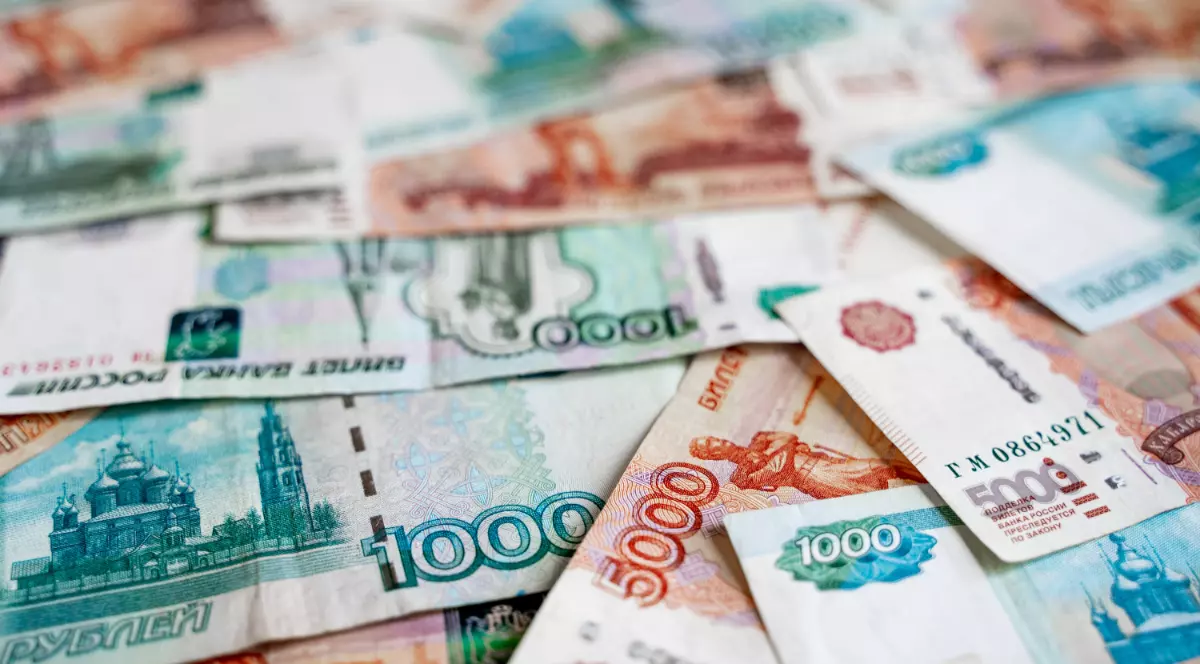 Bancnote de ruble rusesti, de culoare portocaliu, albastru și verde, de diferite valori, împrăștiate pe o suprafață