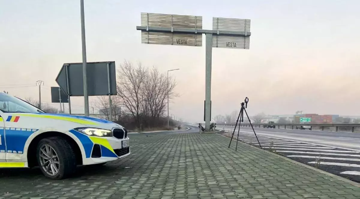 sistem radar pe trepied langa o masina de politie, in partea de sus sunt doua indicatoare rutiere de directie