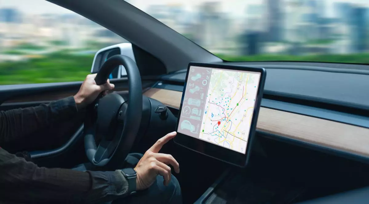 sofer intr-o masina electrica moderna in timp ce seteaza datele de navigare in consola digitala a masinii. in prim plan este prezentat bordul masinii si se observa volanul si un ecran mare pentru navigatie