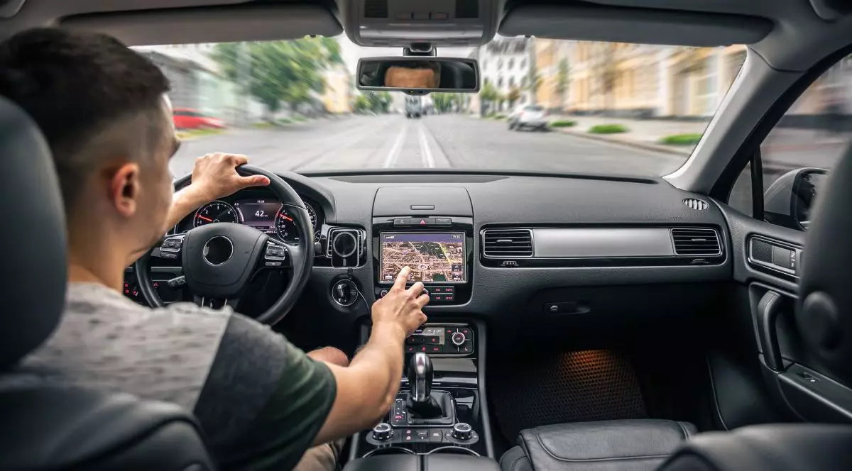 Un bărbat care este la volanul mașinii atinge ecranul unui sistem de navigație GPS