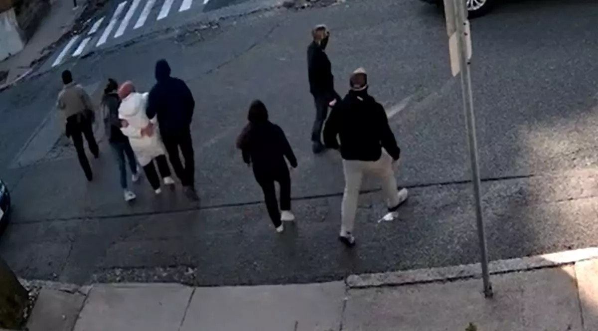 Oameni pe stradă, cu spatele, îmbrăcați în negru, alături de o altă persoană imnrăcată în alb, cu mainile la spate