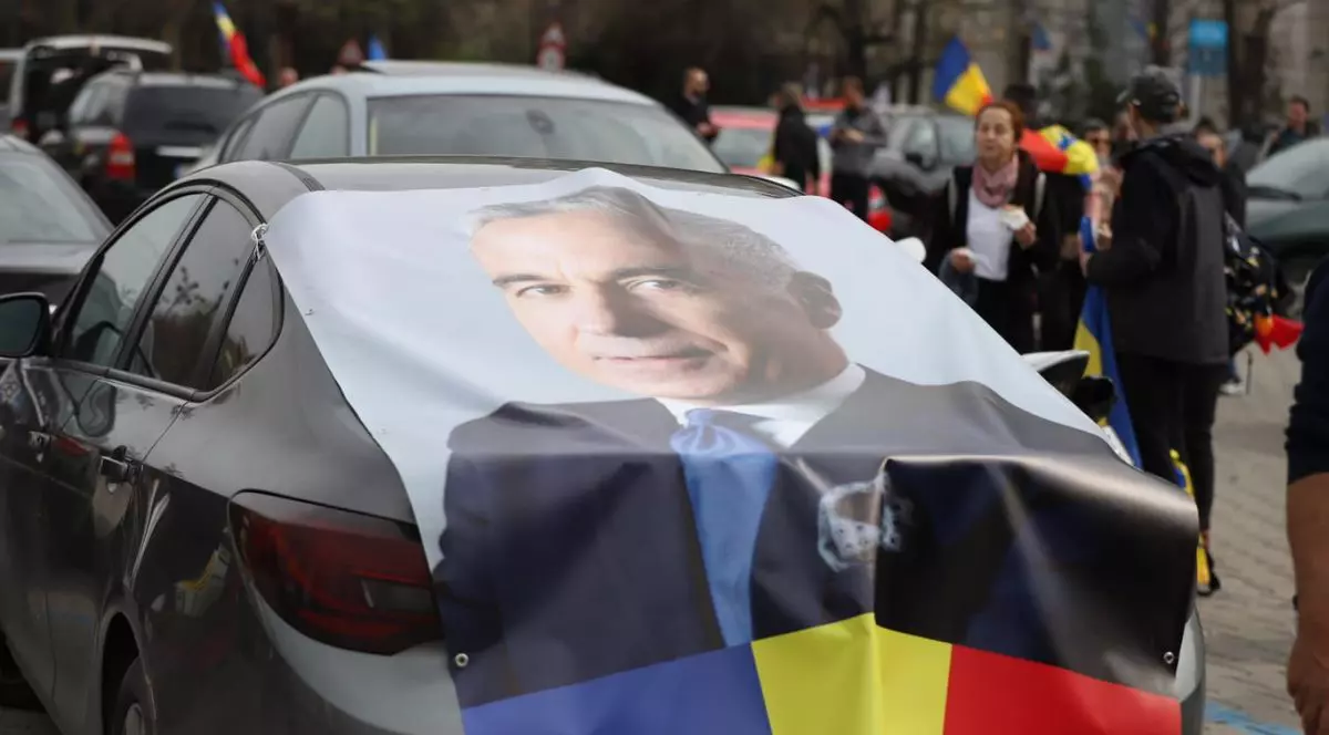 O mașină neagră la protestul din Piața Victoriei, pe care este pus un afiș mare cu Călin Georgescu