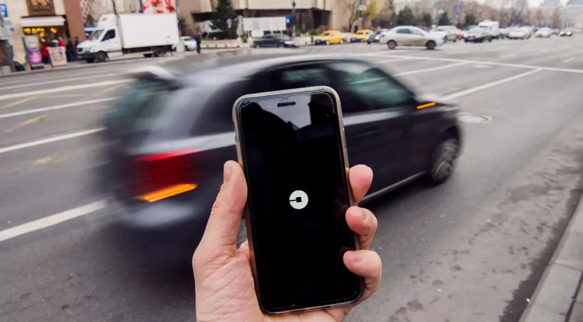 Bărbat care ține un smartphone cu aplicația Uber deschisă și așteaptă o mașină, în București.