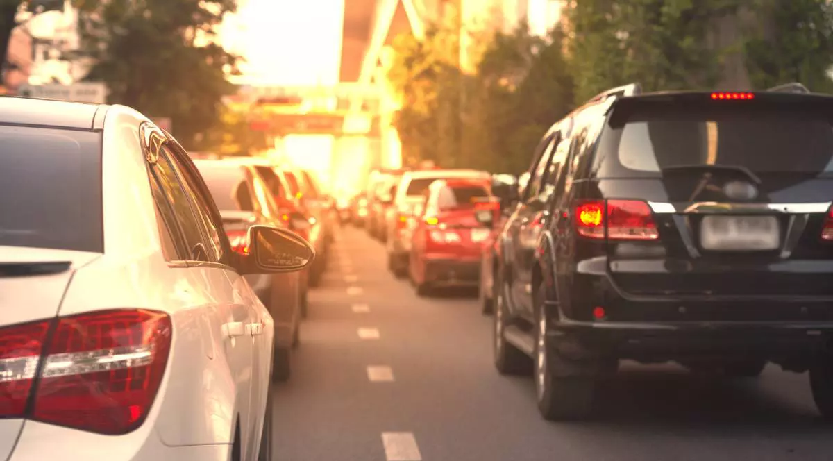 mai multe masini in trafic, pe un drum cu doua benzi pe sens, posibil intr-un oras, in prim plan este o masina neagra