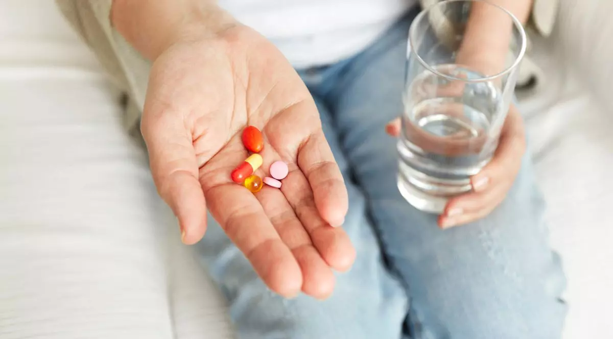 femeie care ține medicamente în palmă și un pahar de apă în mână