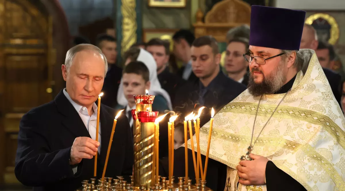 Vladimir Putin- in stanga- în biserică aprinde o lumânare. În dreapta este un preot ortodox