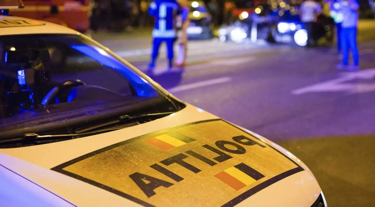 Fotografie în care în prim plan este o mașină a poliției, pe fundal agenți de poliție care fac măsurători în urma unui accident auto.