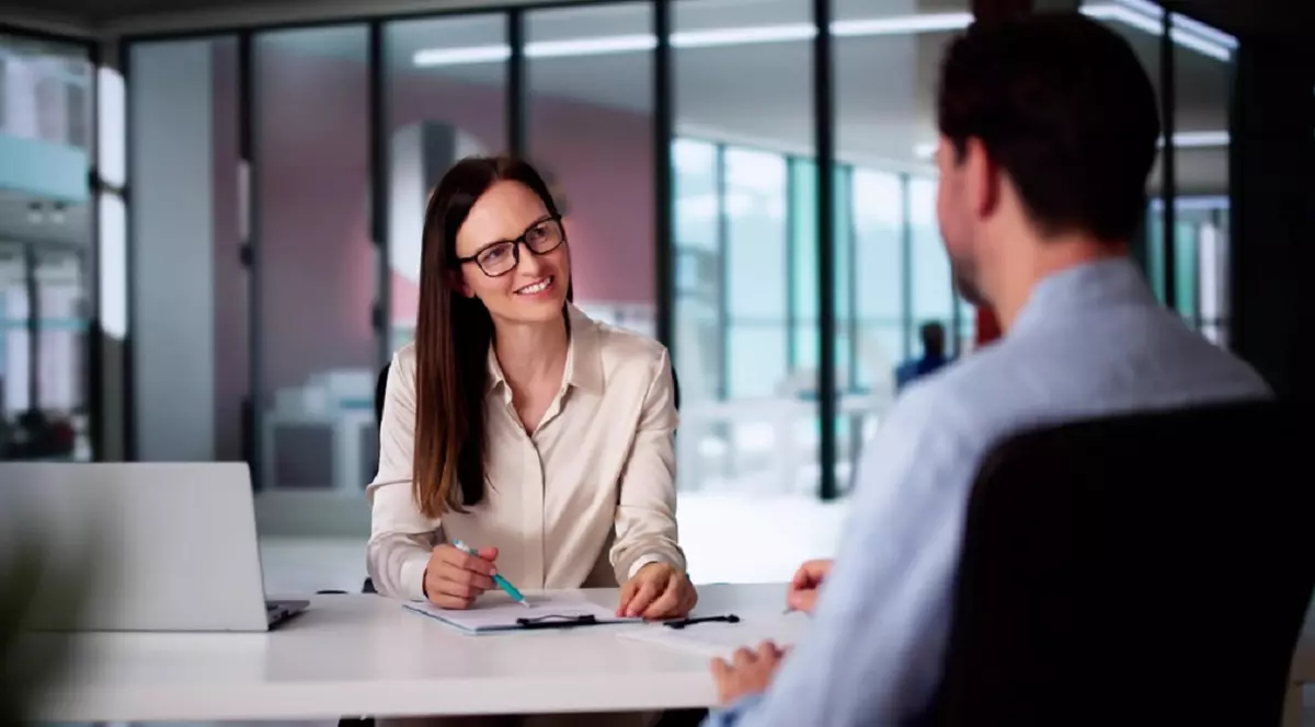 Un barbat, imbracat cu o camasa albastra, se afla la un interviu de job, cu o femeie de la HR, imbracata office cu o camasa alba