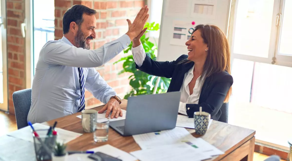 O femeie și un bărbat, la birou, în timp ce bat palma, în timp ce ambii zâmbesc