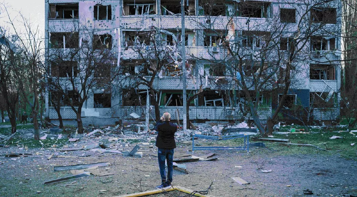 O vedere a unui bloc din Harkov după atacul Rusiei, un loc de joaca in fața căruia un bărbat ăncearca sa pozeze blocul devastat de explozie